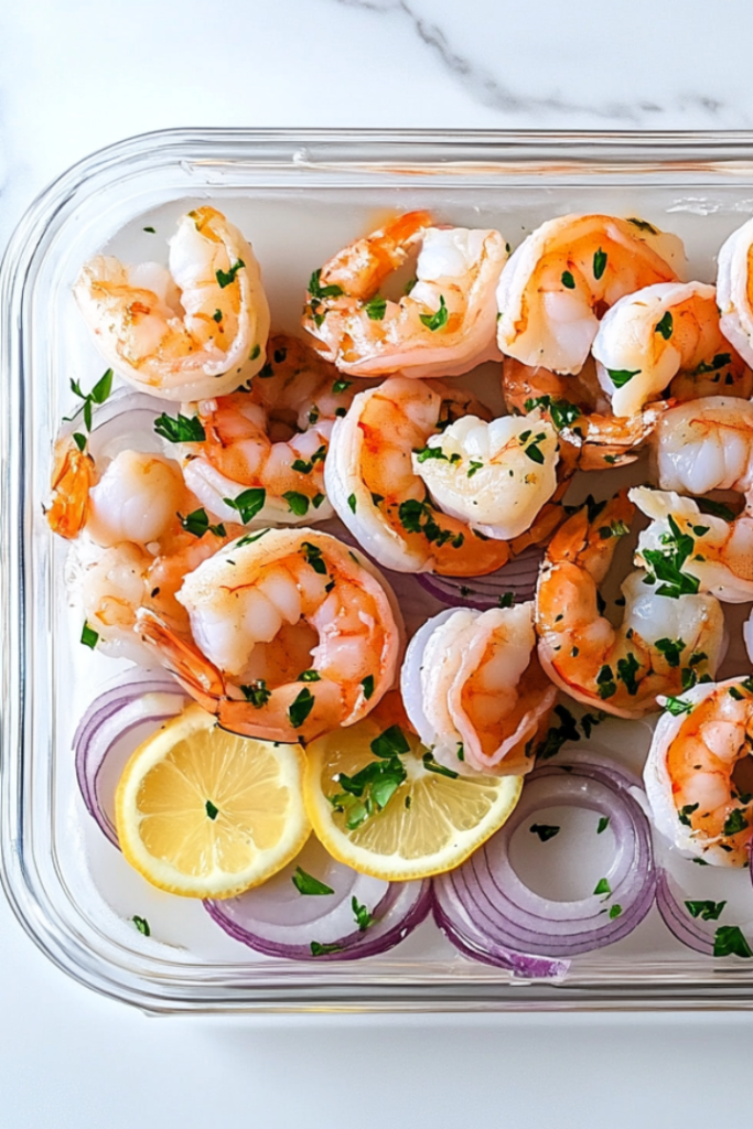 Close-up shot of a chilled serving platter on the white marble cooktop, beautifully arranged with marinated shrimp, lemon slices, and onions. The shrimp glisten with the flavorful marinade, ready to be enjoyed