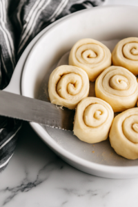 The puff pastry being carefully rolled up into a log, with the edge sealed using a light brush of melted butter