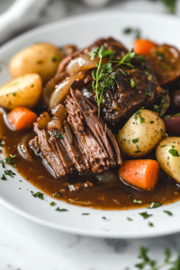A close-up of a serving plate featuring a portion of tender, slow-cooked pot roast surrounded by perfectly cooked carrots, potatoes, and onions. The dish is drizzled with its rich, slow-cooked gravy and garnished with fresh herbs, beautifully presented over the white marble cooktop.