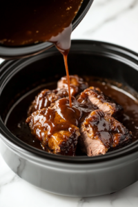 A close-up of a black slow cooker on the white marble cooktop, as a thick, tangy BBQ sauce is poured over the pork shoulder. The rich sauce coats the meat, ensuring deep flavor infusion as it slowly cooks to tender perfection.