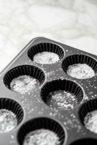 A clean patty pan on the white marble cooktop, lightly coated with cooking oil spray. The spray glistens on the pan’s surface, ready for the next step