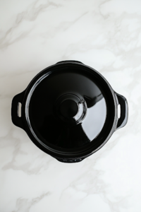 A close-up shot of a black crockpot on the white marble cooktop, lightly sprayed with cooking spray to prevent sticking. The glossy interior reflects the light, ensuring a smooth and even surface for the ham to cook without sticking.
