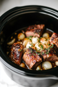 A close-up of a black slow cooker on a white marble cooktop, filled with a bed of freshly chopped onions and crushed garlic. The seared pork shoulder rests on top, ready to absorb the rich, aromatic flavors as it slow cooks.