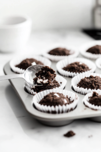 A close-up shot of a cupcake pan lined with liners, where about 1 tablespoon of the Oreo crumb mixture is being pressed firmly into each liner.