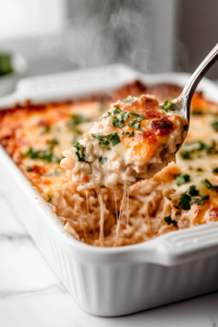 A serving spoon lifts a generous portion of cheesy chicken and rice bake from the glass baking dish. Layers of melted cheese, creamy rice, and tender chicken are visible, with steam rising, showing it's hot and ready to be enjoyed.