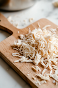 A close-up shot of a wooden cutting board on a white marble cooktop, with imitation crab meat being carefully shredded into thin strips by hand, creating delicate and flaky textures for the kani salad.