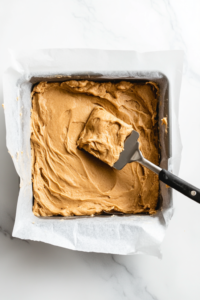 Thick cookie dough being spread evenly into the prepared baking pan, ready for the oven