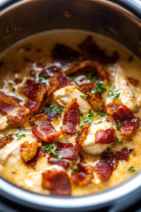 A close-up of crispy, deep golden-brown bacon being sprinkled over the creamy chicken mixture inside the Instant Pot. The crispy texture contrasts beautifully with the rich, cheesy sauce, while fresh herbs add a pop of color and freshness.