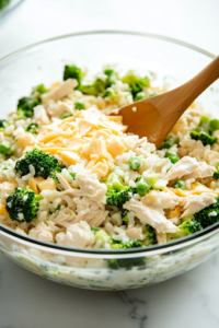A small glass bowl on the white marble cooktop holds freshly steamed, vibrant green chopped broccoli. A fork gently presses into a piece, revealing its tender texture, ready to be mixed into the dish.