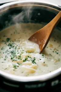 A close-up of the Instant Pot back on 'Sauté' mode, as the thickened creamy sauce bubbles slightly. A wooden spoon stirs the mixture, ensuring even blending while the steam carries the rich aroma of melted cheese and fragrant herbs.
