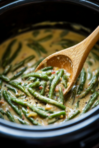 A close-up shot of a wooden spoon stirring the green bean mixture inside the black slow cooker, ensuring the creamy sauce evenly coats the vegetables. The ingredients blend together, creating a smooth and flavorful consistency.