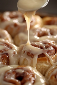 A spoon drizzling a smooth, pink strawberry glaze over the warm rolls, ready to be enjoyed.