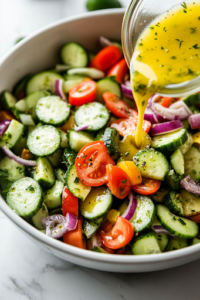 Overhead view of the freshly made dressing being poured over a Greek salad, with a spoon gently tossing the ingredients to ensure even coating of the dressing on the veggies and feta.
