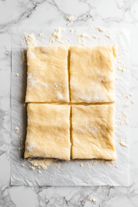 A sheet of crescent roll dough laid flat on a floured surface, separated into four rectangles. The perforations are pinched together to seal the seams
