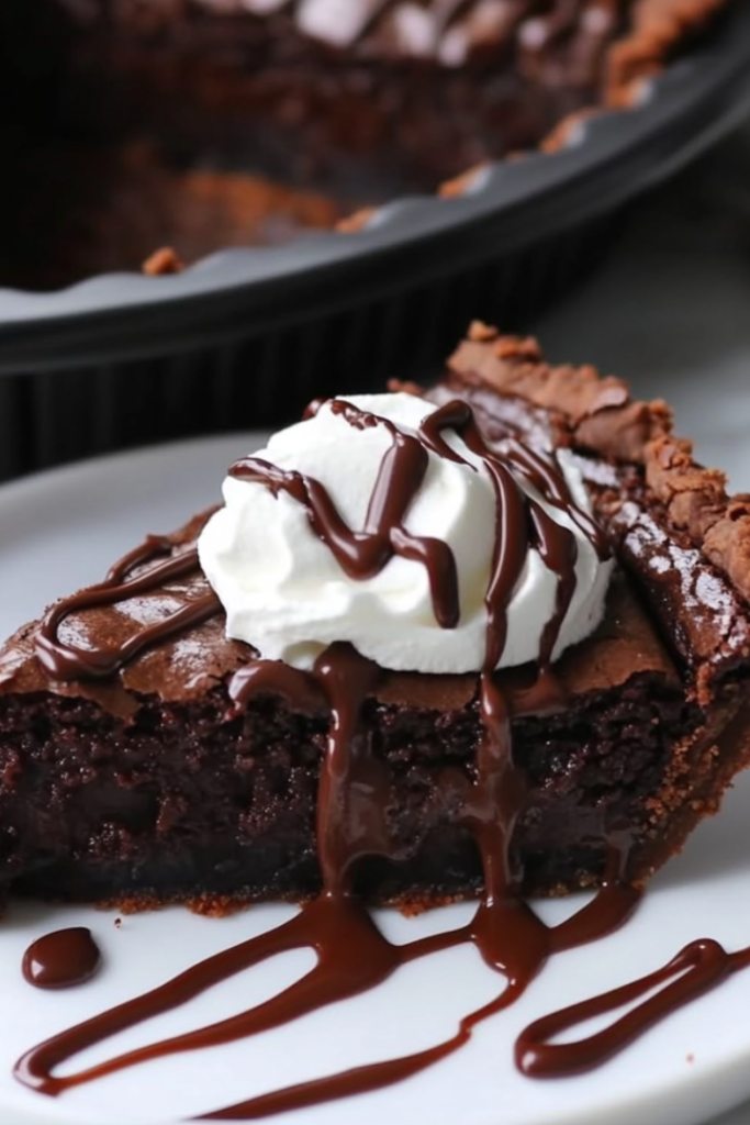 Close-up shot of a sliced piece of vegan brownie pie on a white marble plate, topped with a swirl of vegan whipped cream and drizzled with melted chocolate. The rest of the pie remains in the black pie pan, ready to be served.