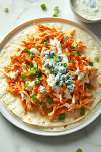 A freshly assembled Buffalo chicken taco sits on a white plate over the white marble cooktop. The warm tortilla is filled with spicy Buffalo chicken, creamy coleslaw, crumbled blue cheese, and sliced green onions. A small bowl of ranch dressing is placed beside it for dipping, completing the delicious dish.