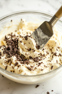 Heavy cream and powdered sugar being whipped together in a mixing bowl to stiff peaks.