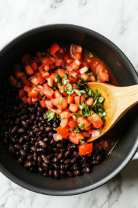 A black skillet on a white marble cooktop with olive oil sizzling as chopped onion, minced garlic, diced poblano, Yukon gold potatoes, and fresh corn are being sautéed. Steam rises as the ingredients soften.