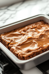 Warm caramel frosting being poured over cooled cookie bars, with a spatula spreading it evenly