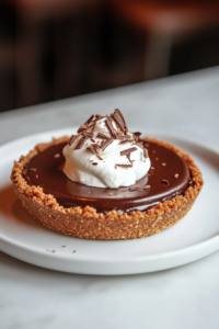 A chocolate pie on a white plate, placed on a white marble countertop. A dollop of whipped cream rests on top, with chocolate shavings sprinkled over the rich, velvety filling.