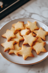 A serving plate with golden shortbread cookies on the white marble cooktop,