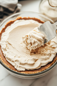 Close-up shot of ladyfingers being dipped into the Kahlua mixture and carefully arranged in the bottom of the cooled crust. The mascarpone mixture is then spread evenly over the ladyfingers.