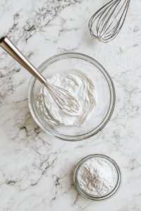 Heavy cream and powdered sugar being whipped together in a mixing bowl to stiff peaks.