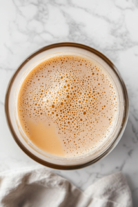 A close-up of a glass mixing bowl on a white marble cooktop, containing warm milk, active dry yeast, and honey. Tiny bubbles form on the surface as the yeast activates, signaling the beginning of the dough-making process.