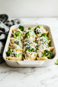 A greased baking dish on a white marble cooktop, neatly arranged with stuffed pasta shells. Each shell is nestled perfectly, ready to be smothered in creamy Alfredo sauce before baking.