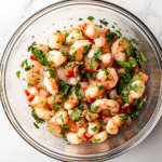 A close-up shot of the completed shrimp ceviche in a glass bowl over the white marble cooktop. The ingredients are well mixed, garnished with extra cilantro, and served with a side of tortilla chips and hot sauce.