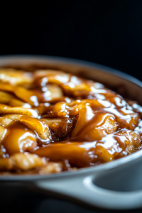 A close-up of the baking dish inside the oven, where the Caramel Apple Cinnamon Roll Bake is turning golden brown and bubbling around the edges. Warm caramel drizzles over the soft rolls, creating a perfectly gooey texture.