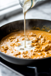 A stainless steel pot on a white marble cooktop holds boiling salted water with long bucatini pasta submerged inside. Steam rises as the pasta softens, while tongs rest nearby for stirring.