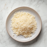 A black saucepan on a white marble cooktop, with fluffing the perfectly cooked Bomba rice. The grains appear light and ready to be served.