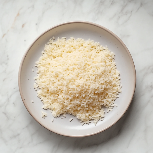 A black saucepan on a white marble cooktop, with fluffing the perfectly cooked Bomba rice. The grains appear light and ready to be served.