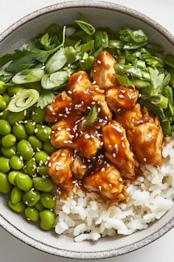 A close-up shot of the final plated Spicy Sesame Chicken Rice Bowl on a white marble cooktop, showcasing a vibrant dish of fluffy rice, crispy golden chicken, edamame, and fresh toppings, all ready to be enjoyed immediately.