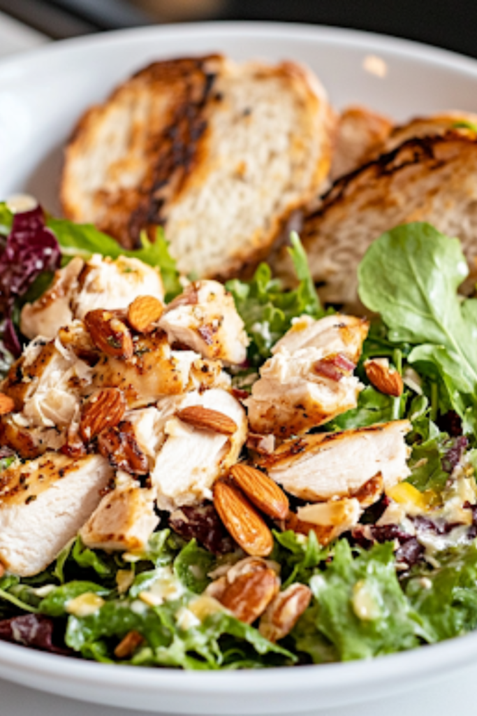 A close-up shot of a serving plate on a white marble cooktop, featuring a sandwich made with creamy almond chicken salad, fresh greens, and toasted bread, ready to be enjoyed.
