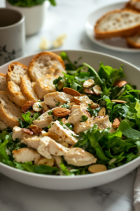 A close-up shot of a serving plate on a white marble cooktop, featuring a sandwich made with creamy almond chicken salad, fresh greens, and toasted bread, ready to be enjoyed.