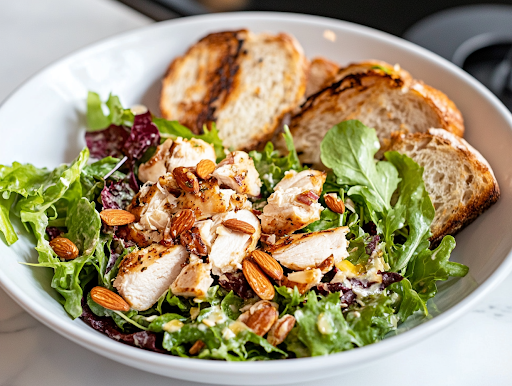 A close-up shot of a serving plate on a white marble cooktop, featuring a sandwich made with creamy almond chicken salad, fresh greens, and toasted bread, ready to be enjoyed.