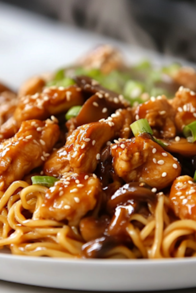 A serving plate on a white marble cooktop, piled high with sesame soy chicken and mushroom noodles. Steam rises from the dish, showcasing the glossy, flavorful noodles ready to be enjoyed.
