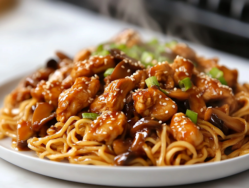 A serving plate on a white marble cooktop, piled high with sesame soy chicken and mushroom noodles. Steam rises from the dish, showcasing the glossy, flavorful noodles ready to be enjoyed.