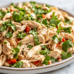 A serving plate on a white marble cooktop showcases the fully mixed Chinese Chicken Salad, bursting with crisp textures and vibrant colors. Fresh herbs garnish the dish, making it ready to be served.