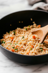 A close-up shot of the black skillet on the white marble cooktop, as the lid is lifted to reveal perfectly cooked dirty rice. The grains are tender, infused with spices, and the broth has been fully absorbed.