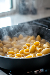 A black pot on the white marble cooktop, filled with boiling salted water. Medium pasta shells are being poured in, creating gentle ripples in the water. Steam rises as the pasta starts to soften, preparing for the salad.