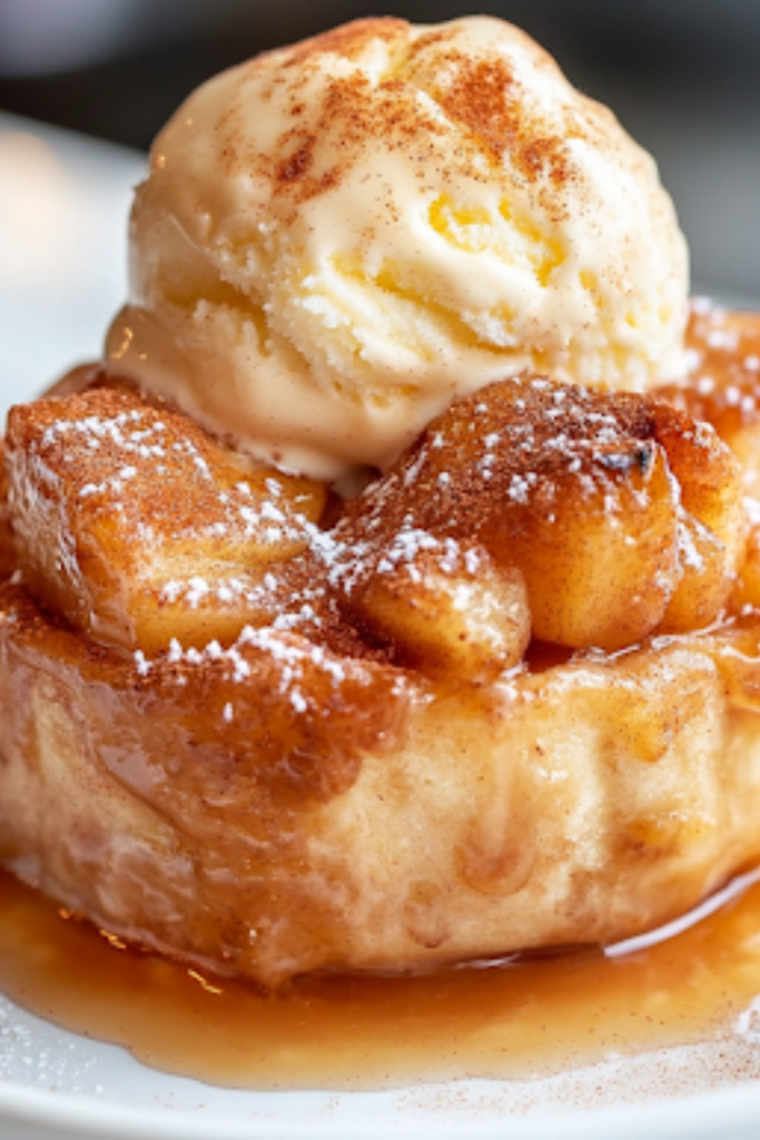 A freshly baked, golden-brown apple dessert resting on the white marble cooktop. The cinnamon-sugar topping glistens, while a scoop of melting vanilla ice cream sits on top, enhancing the warm, spiced flavors.