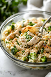 A cooked jumbo pasta shell being carefully filled with the chicken and broccoli mixture using a spoon, resting over a glass bowl on the white marble cooktop. The filling is packed generously for a hearty bite.