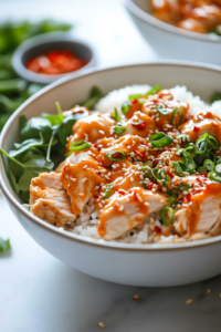 A close-up shot of the final plated Spicy Sesame Chicken Rice Bowl on a white marble cooktop, showcasing a vibrant dish of fluffy rice, crispy golden chicken, edamame, and fresh toppings, all ready to be enjoyed immediately.