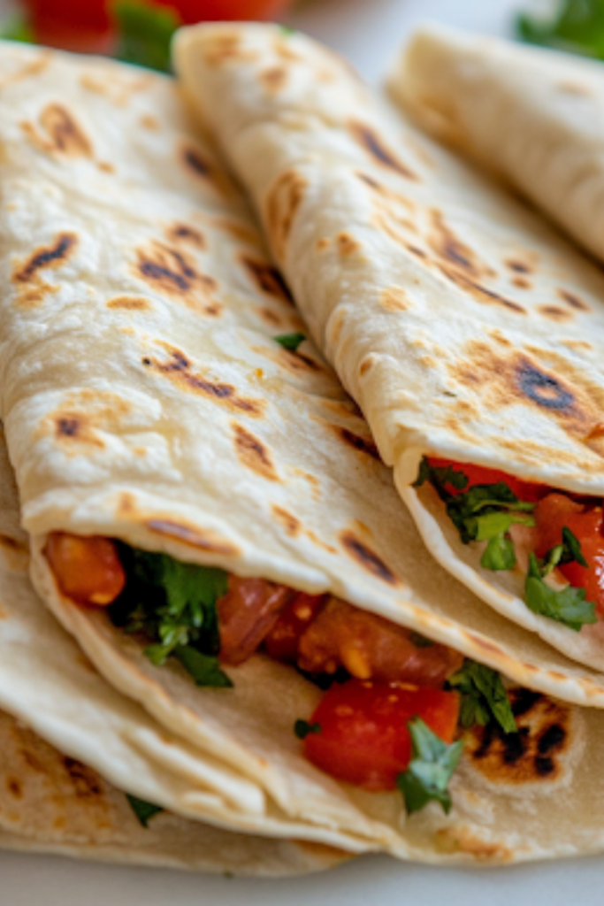 A close-up view of a warm, homemade flour tortilla being folded and filled with delicious ingredients. The tortilla is soft and fresh, making it perfect for serving.