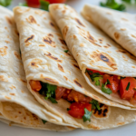 A close-up view of a warm, homemade flour tortilla being folded and filled with delicious ingredients. The tortilla is soft and fresh, making it perfect for serving.