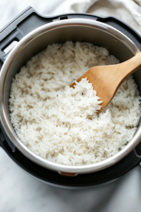 A close-up shot of the Instant Pot inner pot on the white marble cooktop, with a spatula gently fluffing the freshly cooked Calrose rice. The grains appear soft, tender, and slightly sticky, perfect for serving.