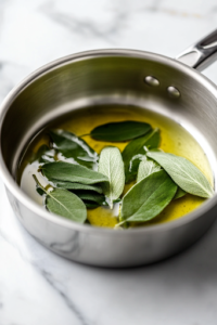 A close-up shot of a small saucepan on a white marble cooktop, where fresh sage leaves sizzle in melted butter. The leaves crisp up as they fry, releasing a fragrant aroma and turning into a perfect garnish for the dish.